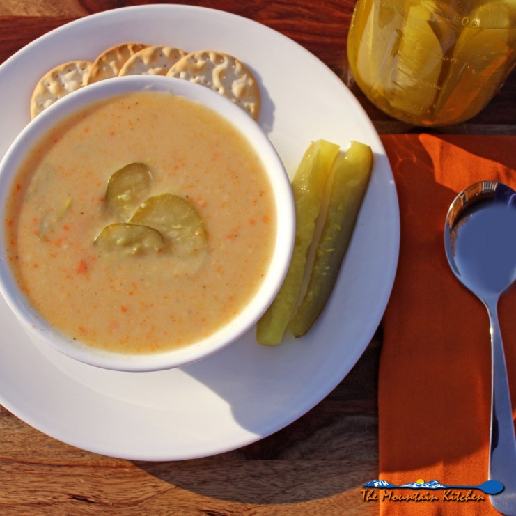dill pickle soup in bowl on a plate with pickles and crackers