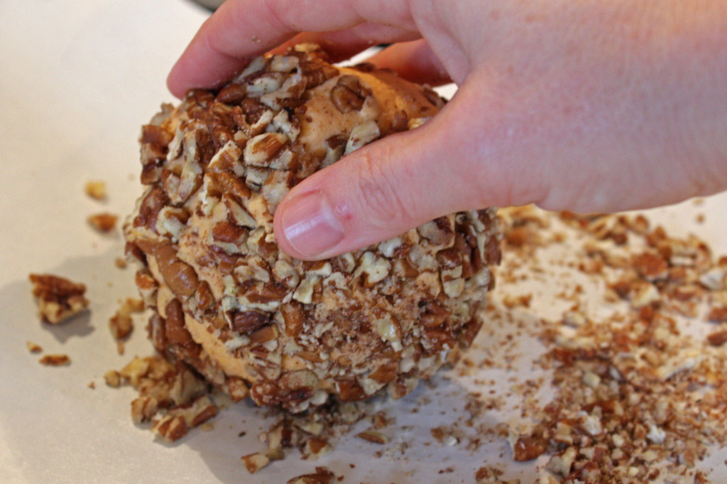 hand rolling Christmas cheese ball in chopped pecans