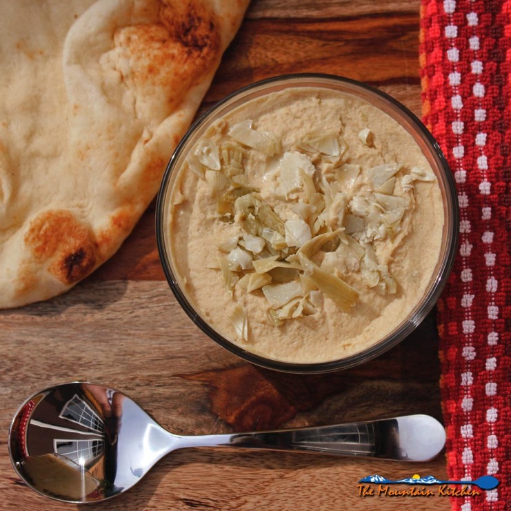Marinated Artichoke Hummus in bowl ready to eat with pita bread and spoon