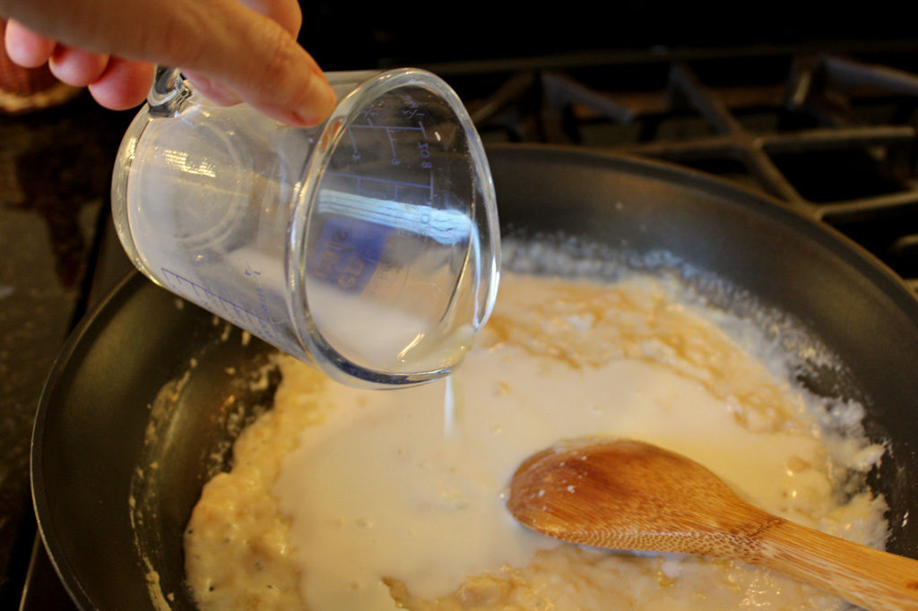 measuring cup pouring milk into roux
