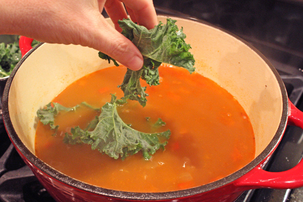 adding kale to pot of soup
