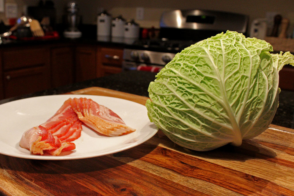 raw bacon on a plate beside head of cabbage