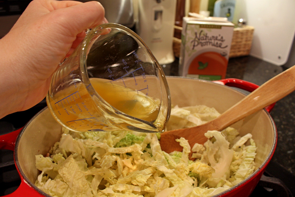 pouring broth into frying cabbage