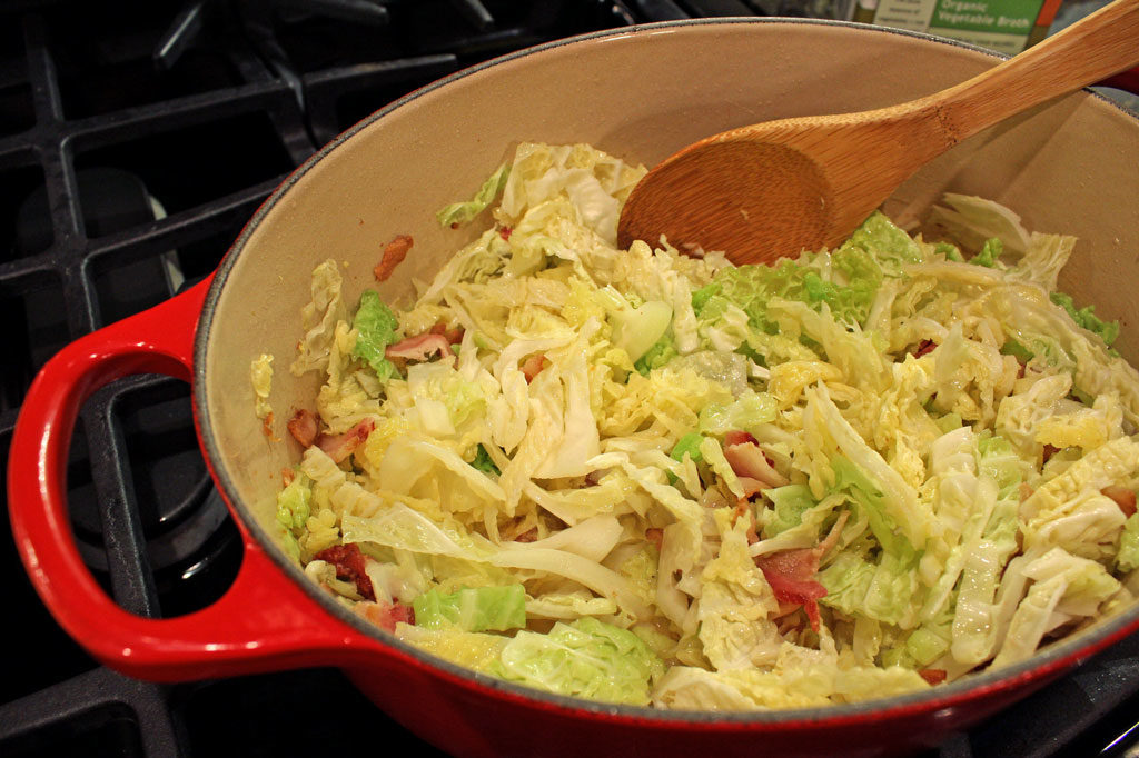fried cabbage with bacon in a Dutch oven with spoon