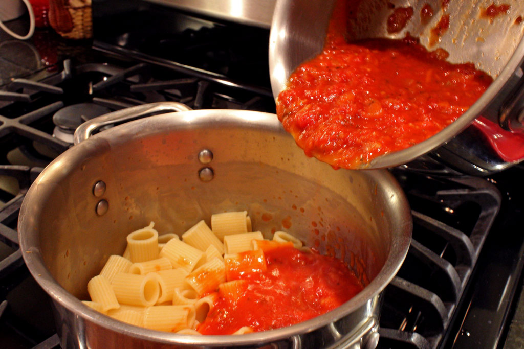 pouring tomato sauce into pasta