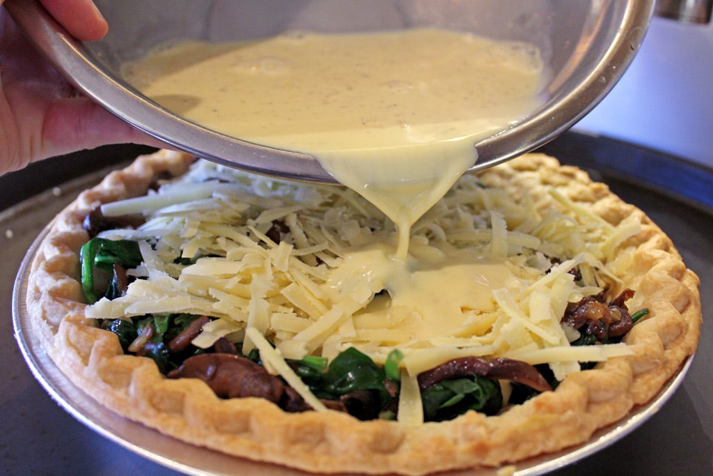 pouring custard into pie crust with veggies and cheese