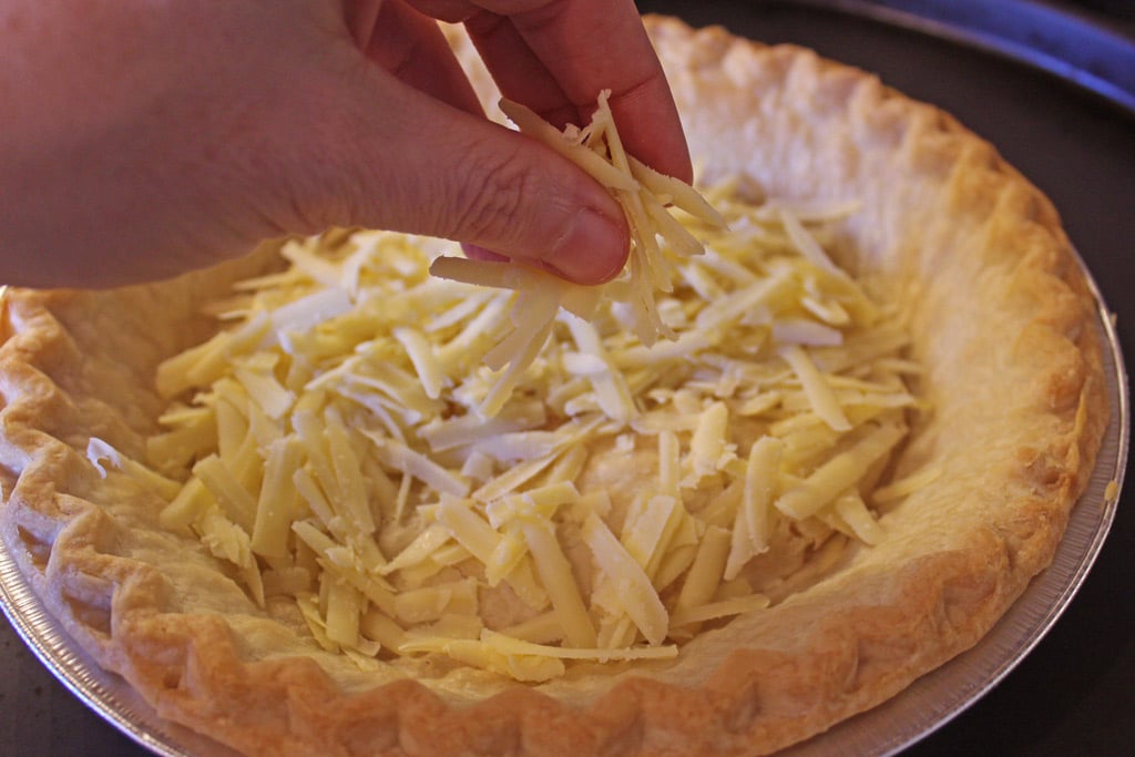fingers dropping cheese into pie crust