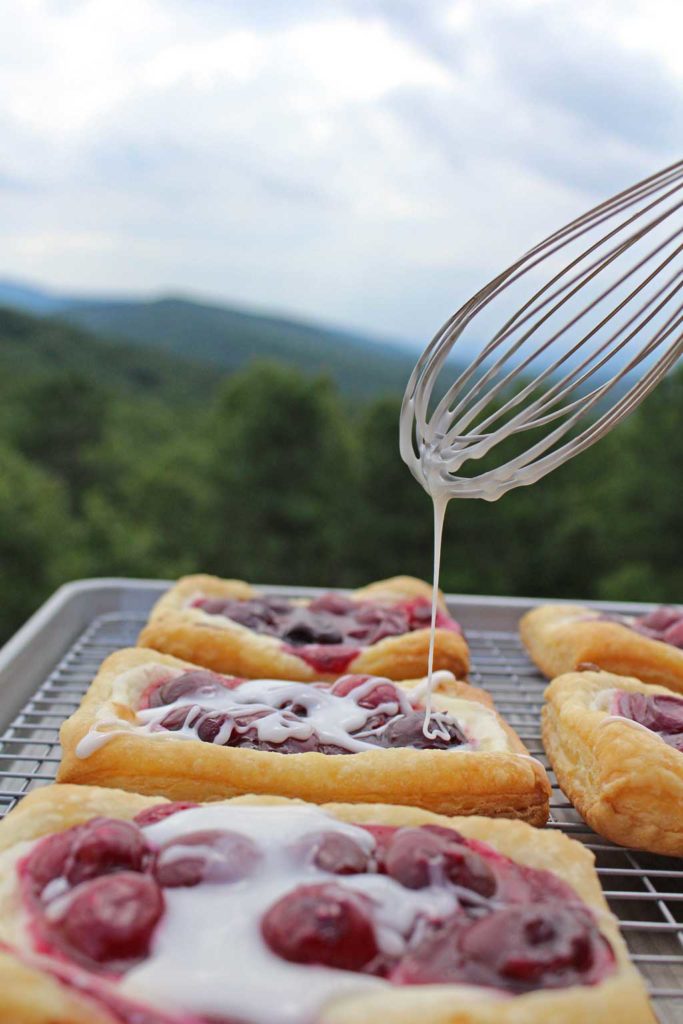 whisk drizzling vanilla glaze over cherry danish