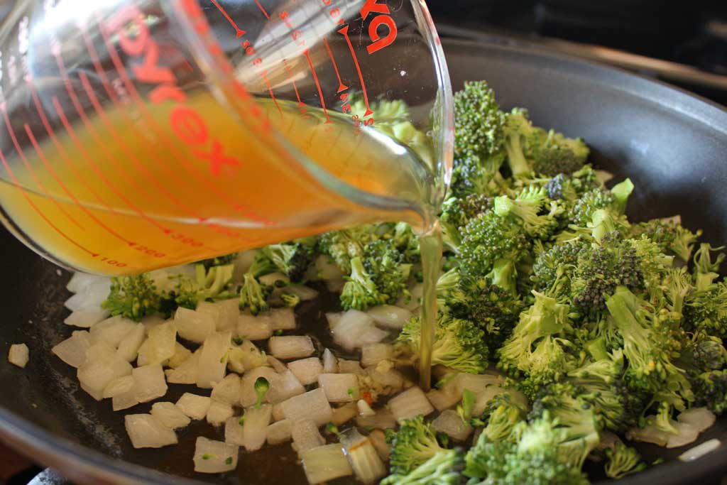pouring vegetable broth into broccoli and onions