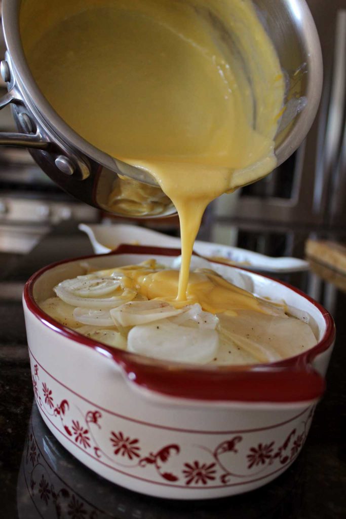 pouring cheese sauce over the potato slices