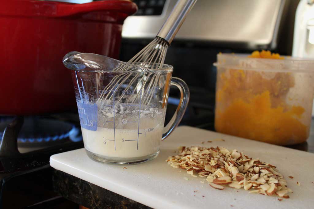 measuring cup with whisk and almonds on cutting board
