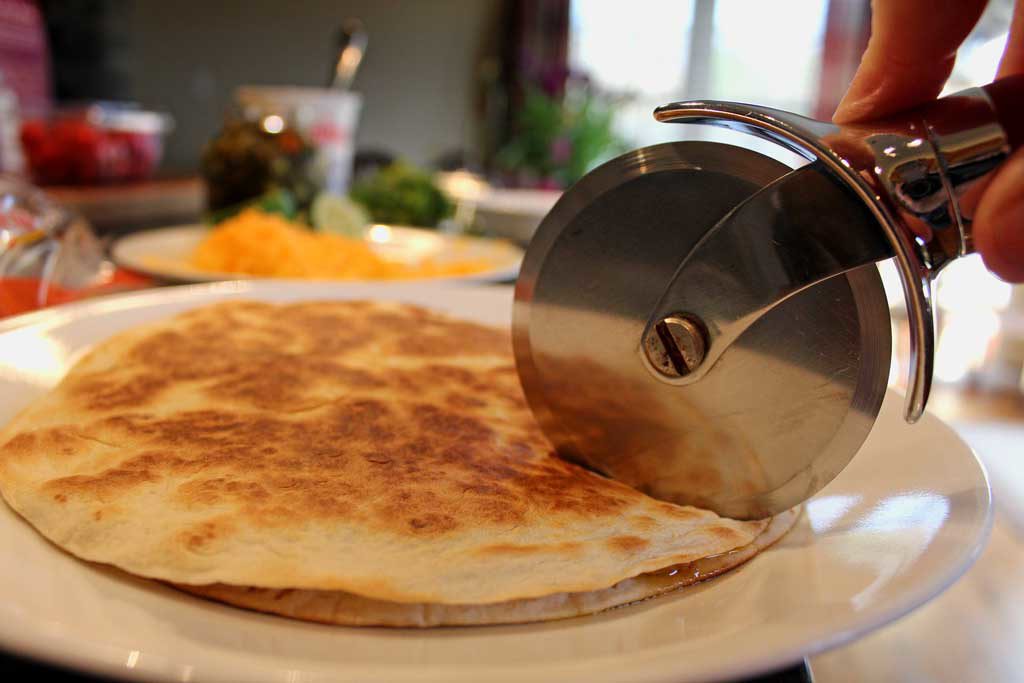 cutting refried bean and cheese quesadilla with pizza cutter