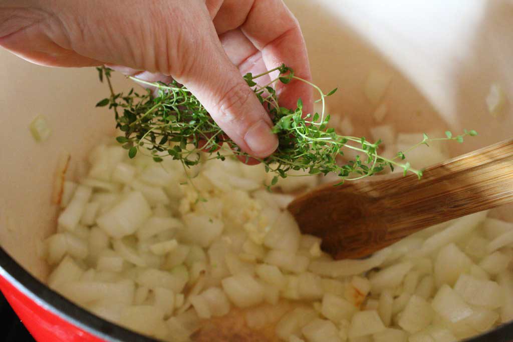 putting thyme into the pot of sauteing onions