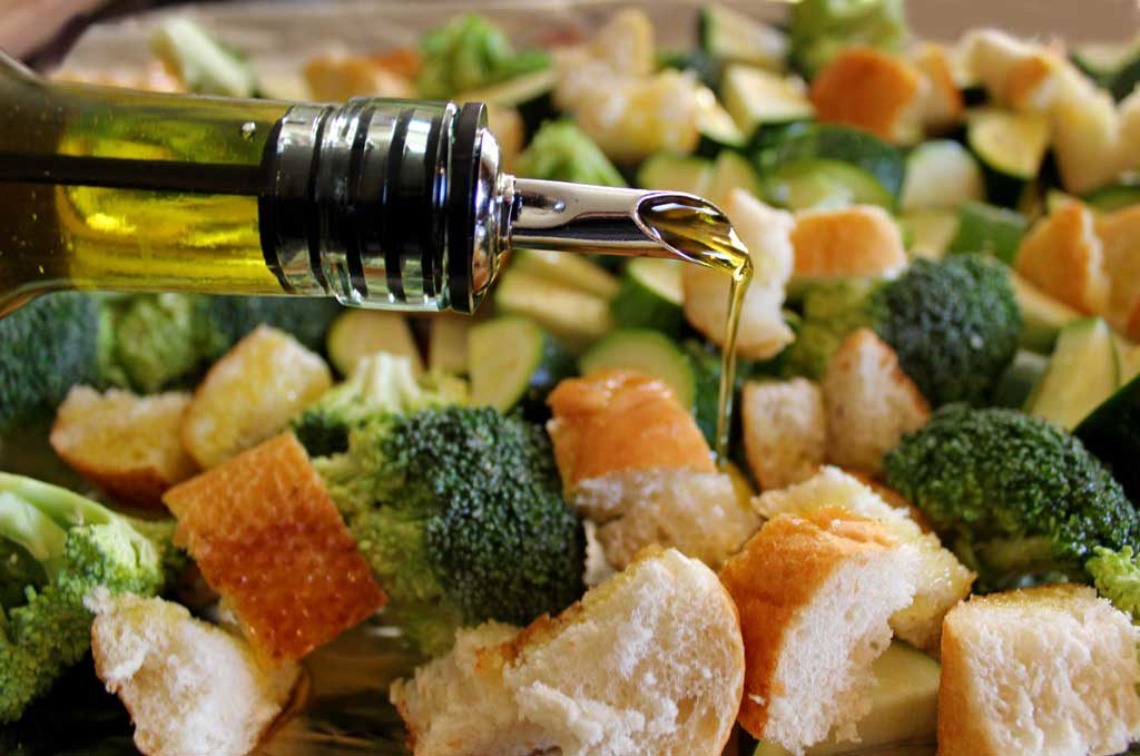 drizzling oil onto sheet pan of vegetables and bread