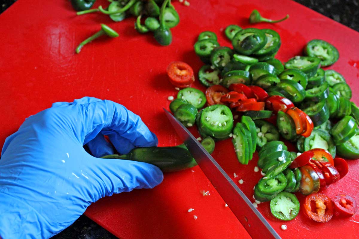 hands wearing gloves slicing jalapenos