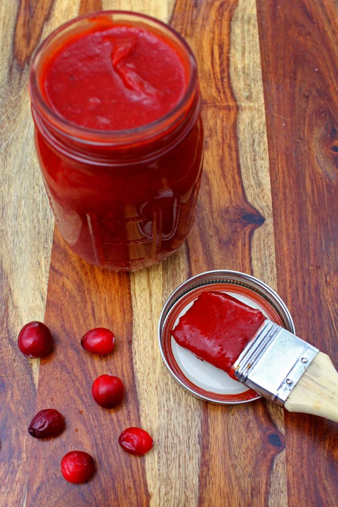 cranberry BBQ sauce on cutting board with basing brush and extra cranberries