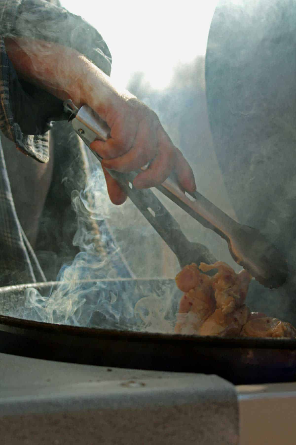 David's hand dropping chicken wings on the grill with tongs