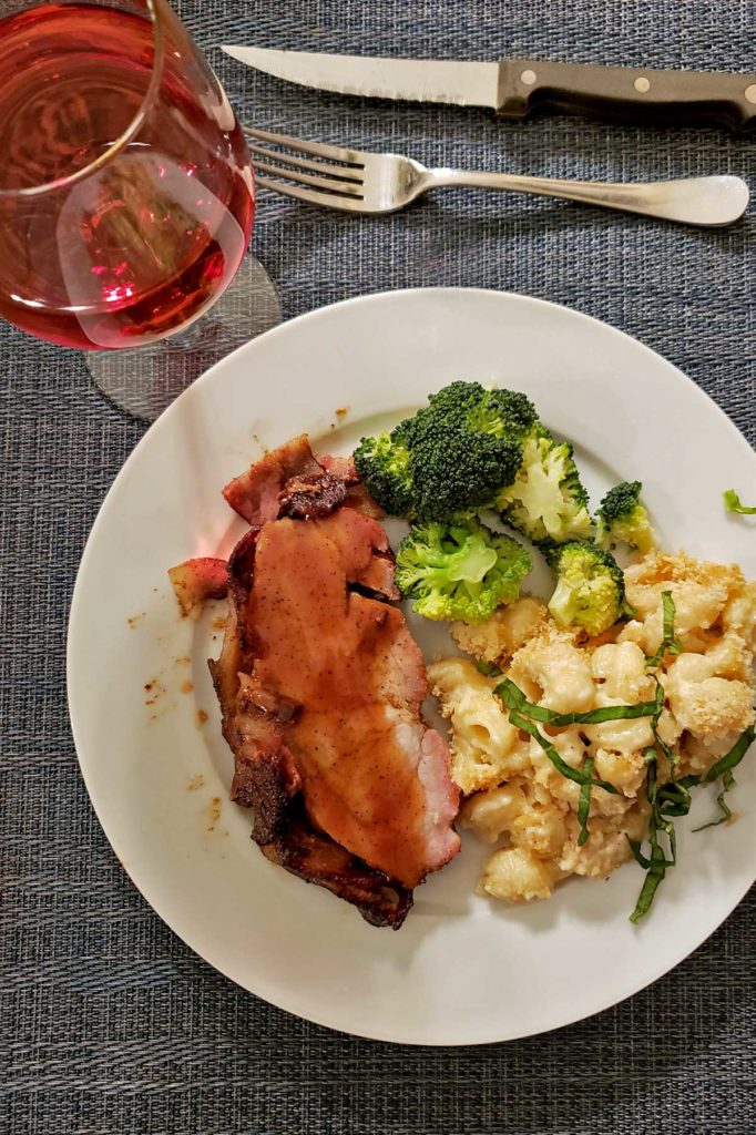 sliced smoked pork loin on a plate with mac and cheese and broccoli and a glass of wine