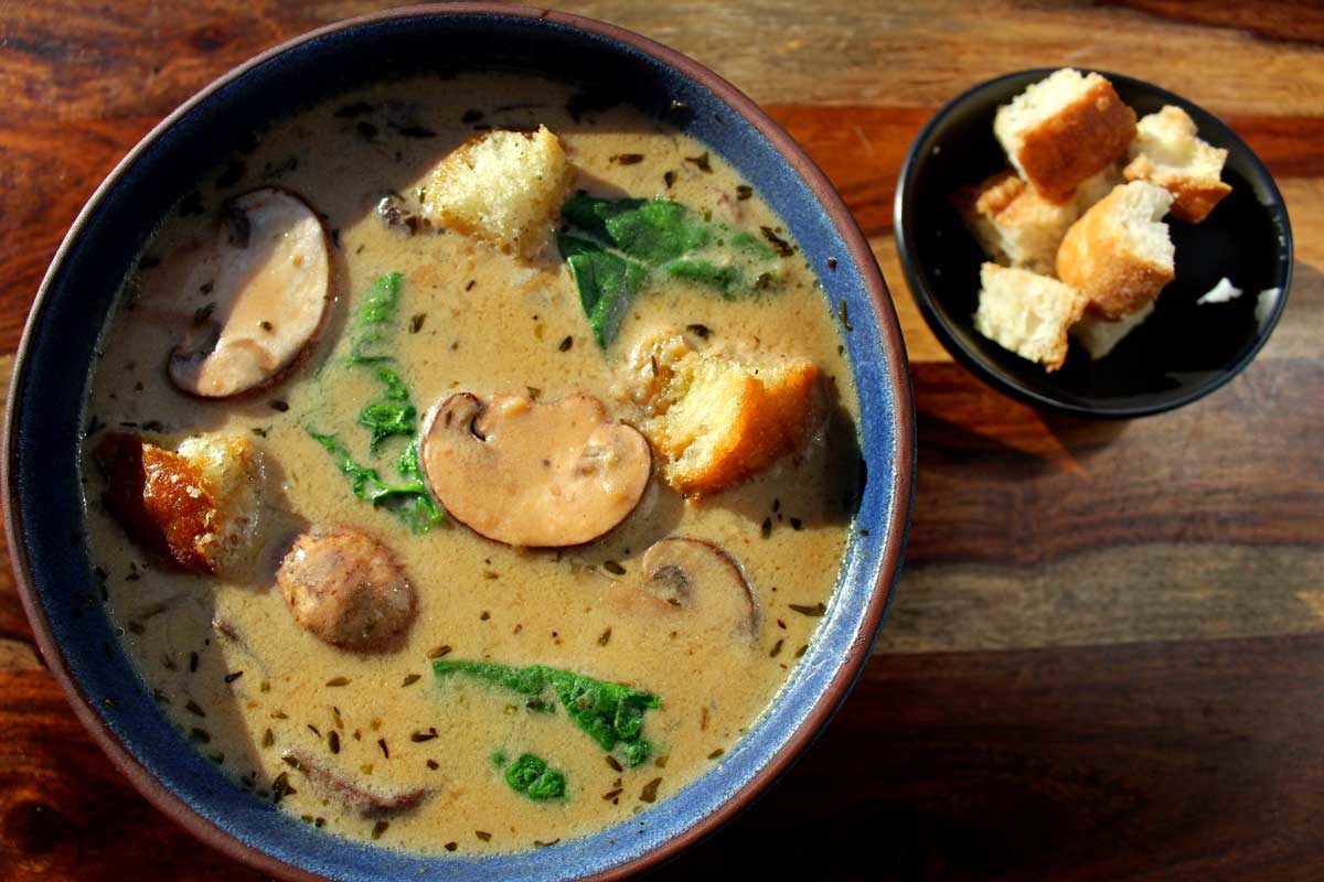 a bowl of mushroom spinach soup and a bowl of croutons