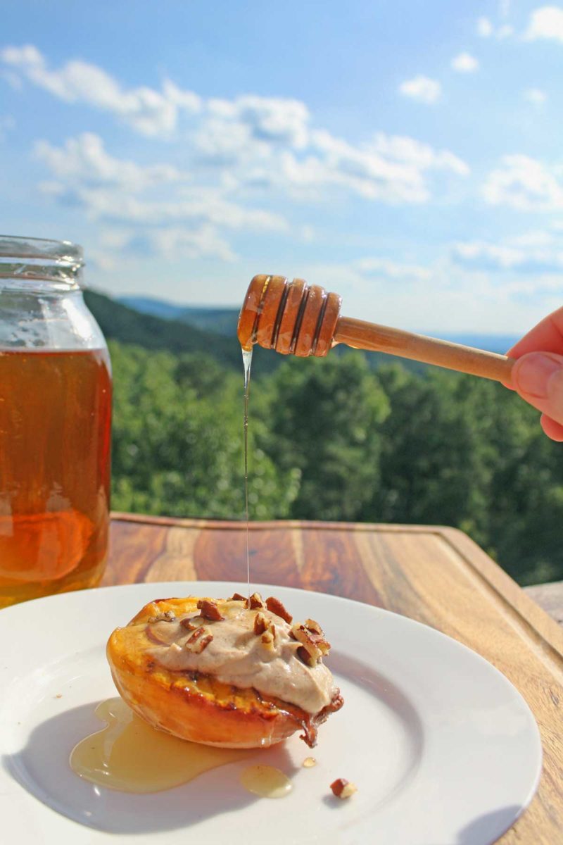 drizzling honey onto peach with mountain view