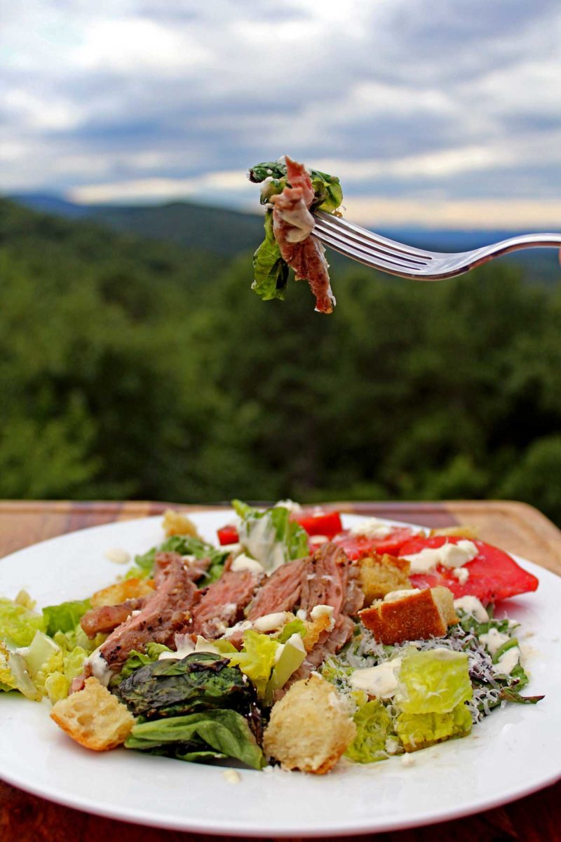 a bite of grilled steak Caesar salad with mountain view