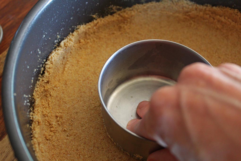 measuring cup pressing graham cracker crust