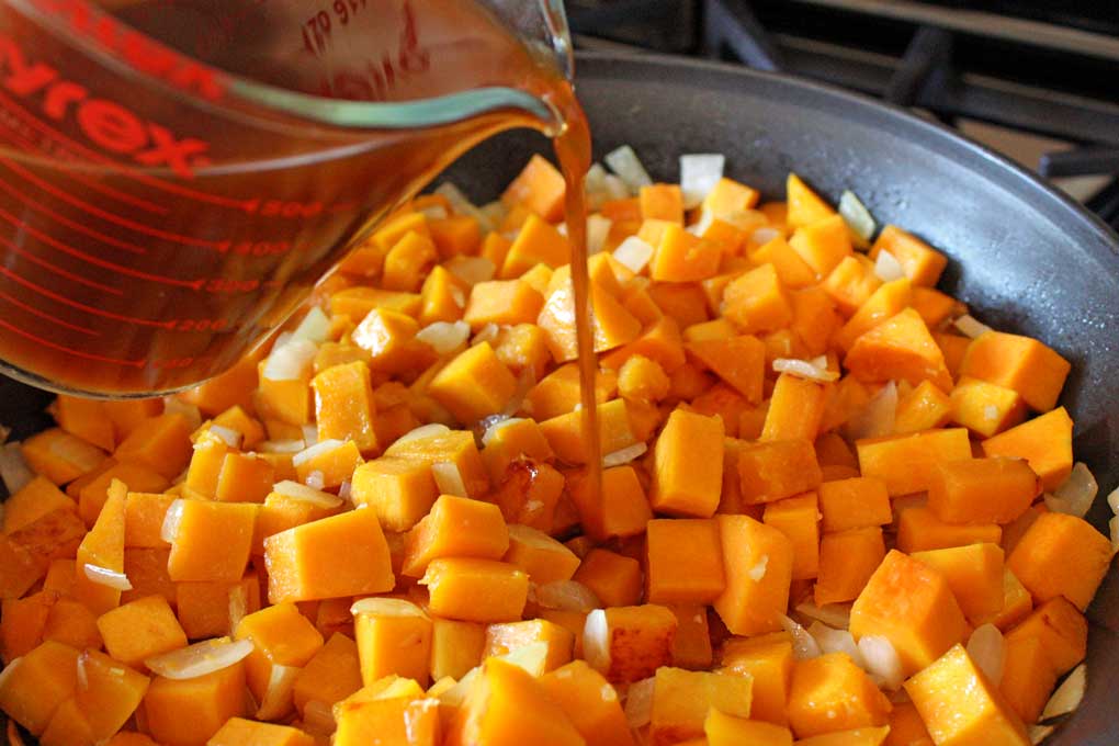 adding vegetable broth to squash mixture in skillet