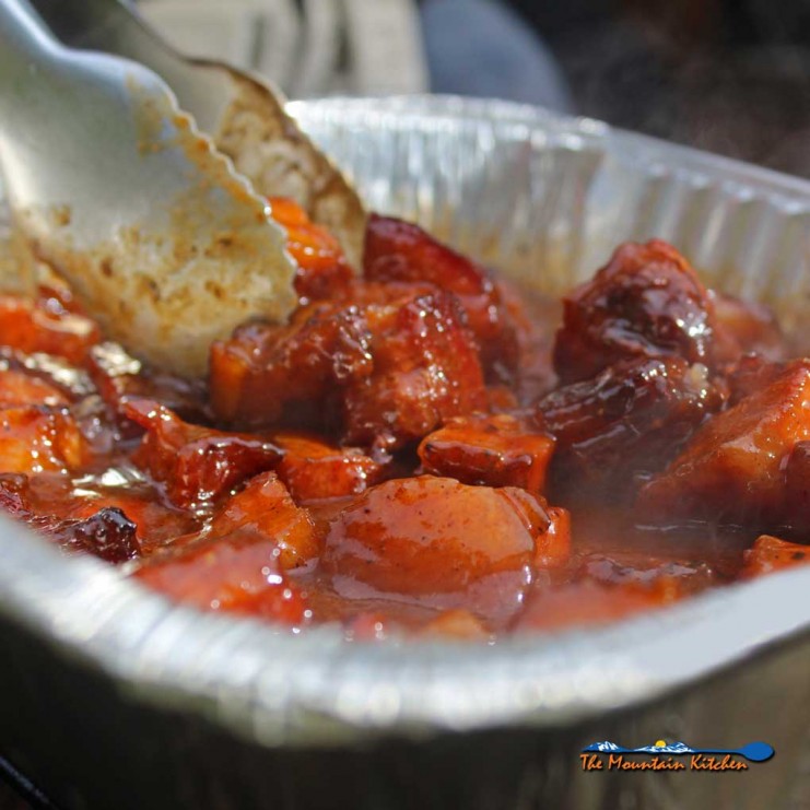 tossing smoked pork belly burnt ends in sauce on grill