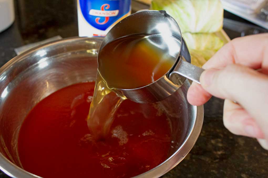 pouring broth into tomato sauce