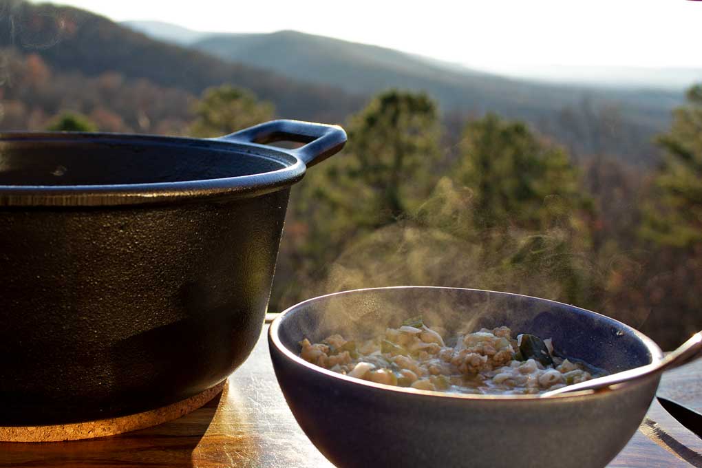 pot of white bean and pork chili with steaming bowl and mountain view