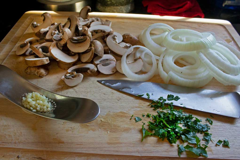 mushrooms, onion, parsley and garlic chopped on cutting board