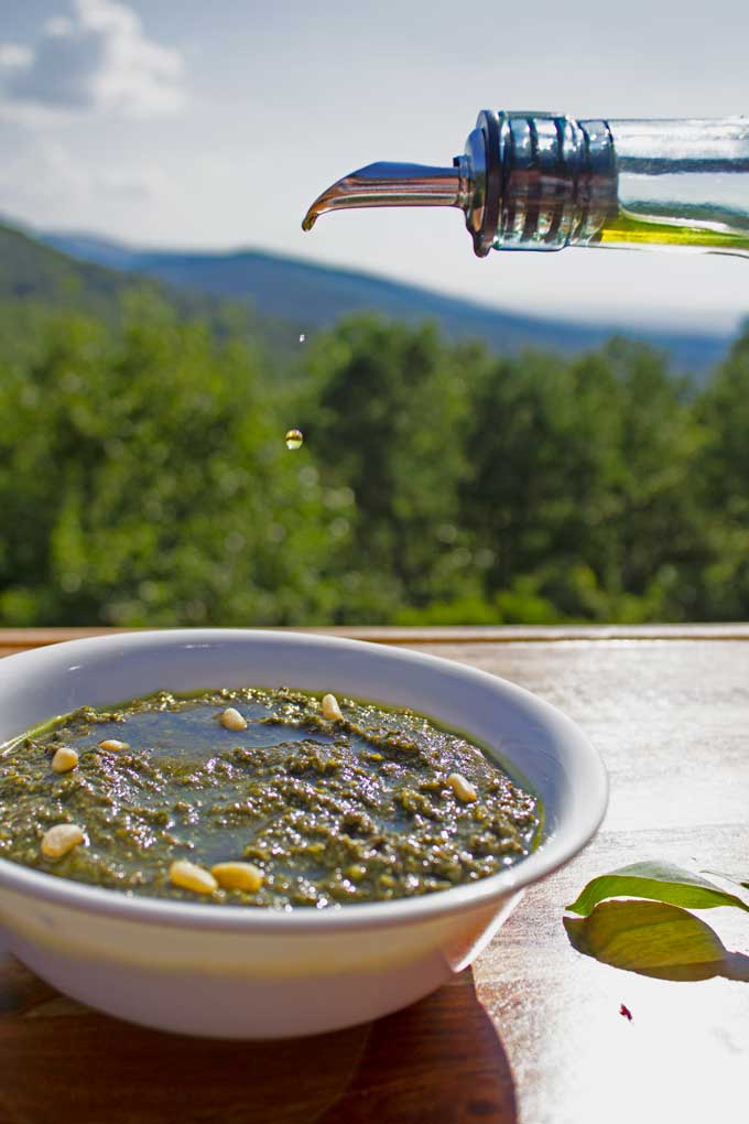 drizzling olive oil into bowl of pesto with mountain view