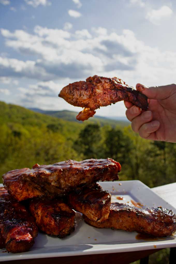 hand holding grilled country-style pork rib over platter of ribs