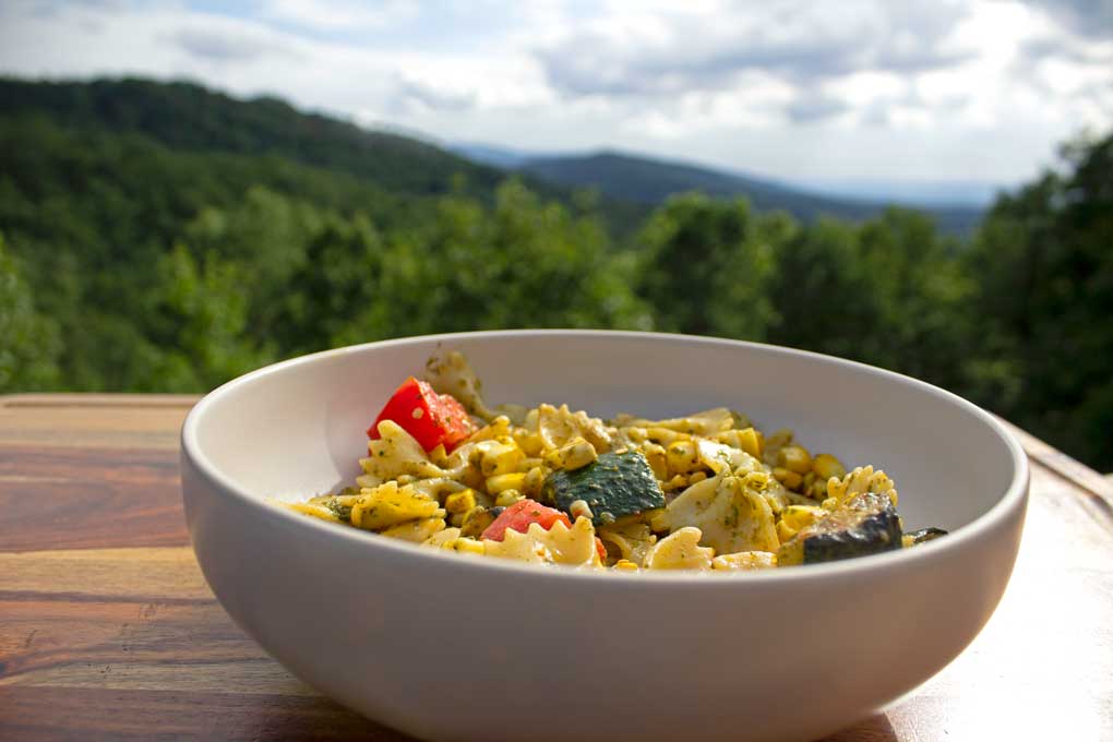 pesto pasta with summer vegetables in bowl with mountain view