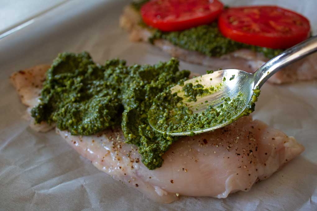 spreading pesto onto chicken with spoon