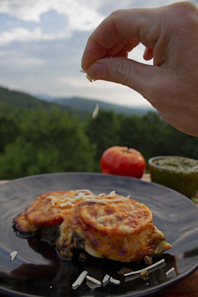 sprinkling cheese onto pesto baked chicken with mountain view
