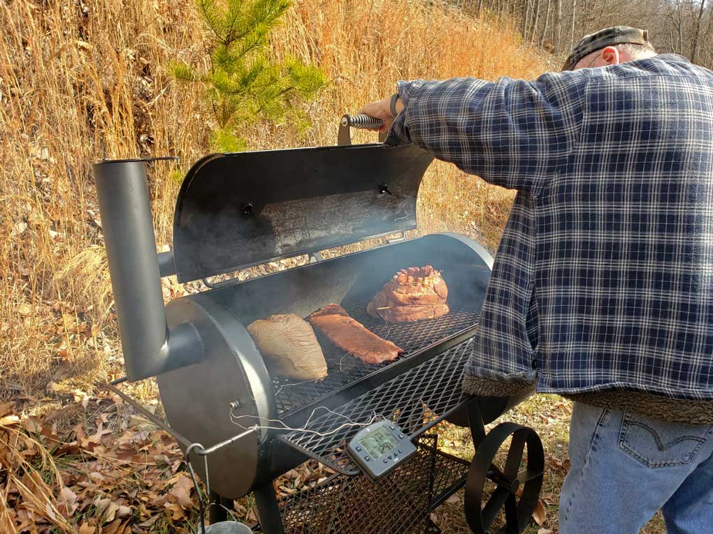 David opening smoker with several pieces of meat on it