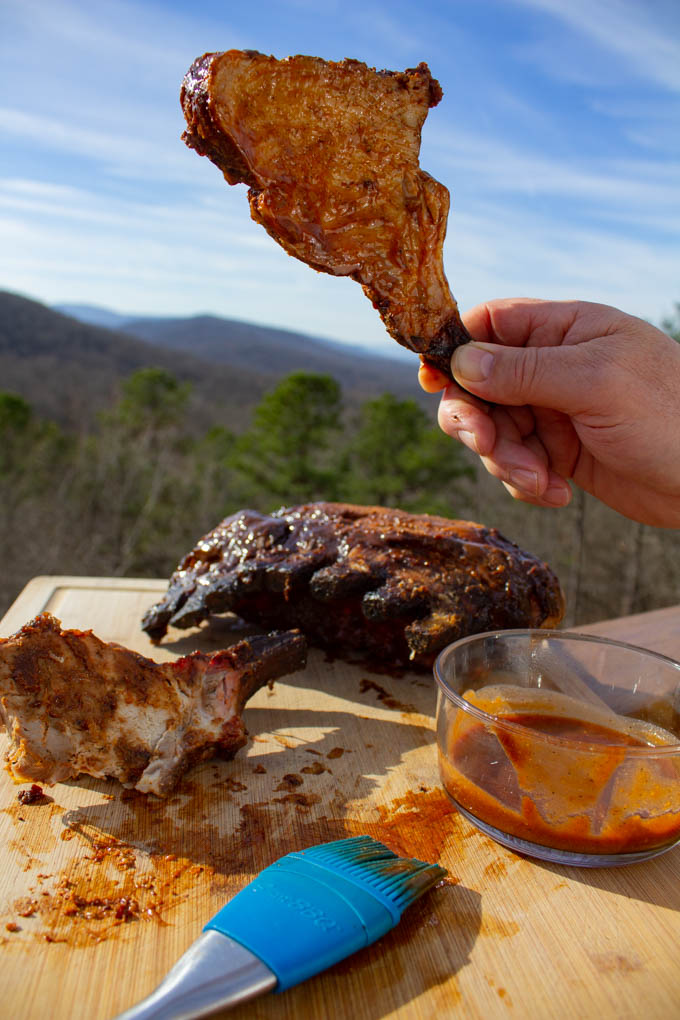 hand holding up chop from the smoked pork crown roast with mountain view