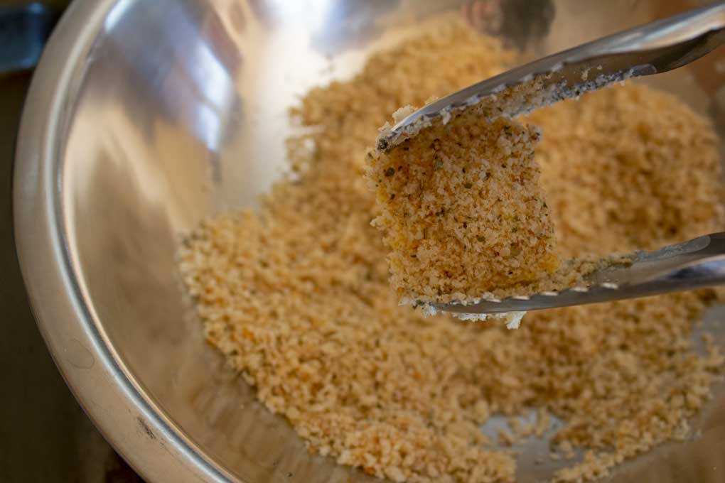 tongs dipping ravioli into breadcrumb mixture