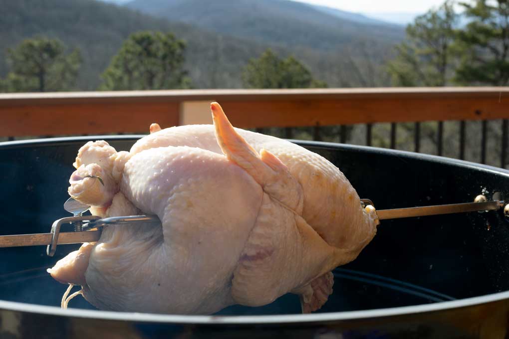 raw chicken spinning on rotisserie with mountain view