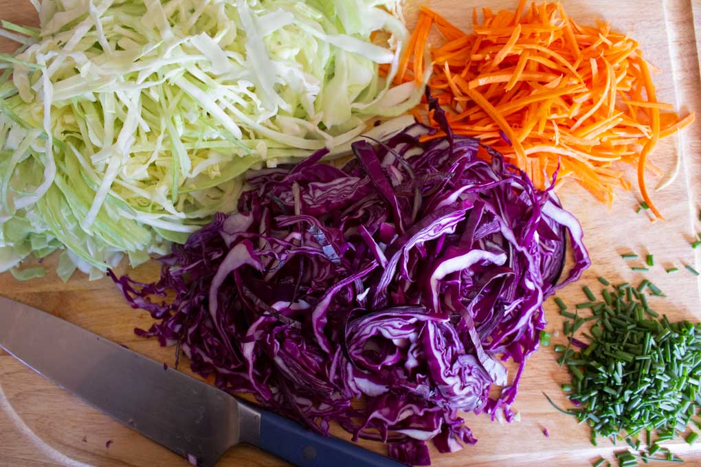 chopped cabbage carrots and chives on cutting board with knife