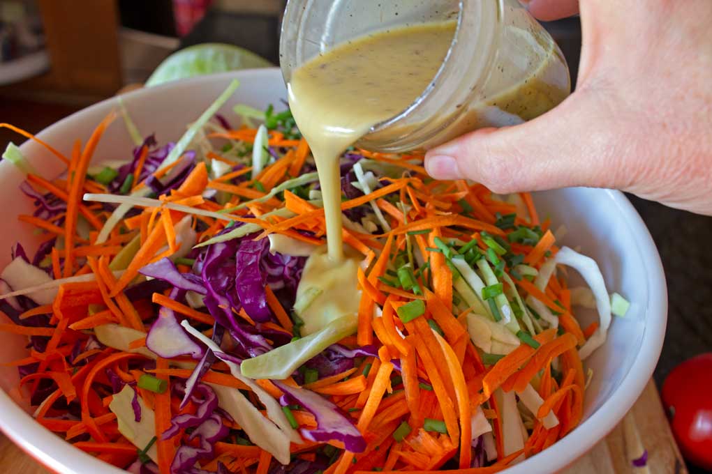 pouring coleslaw dressing over vegetables in bowl
