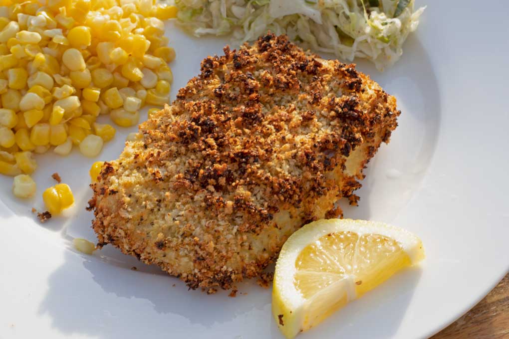 prepared air fryer cod on plate with lemon wedge, corn and slaw