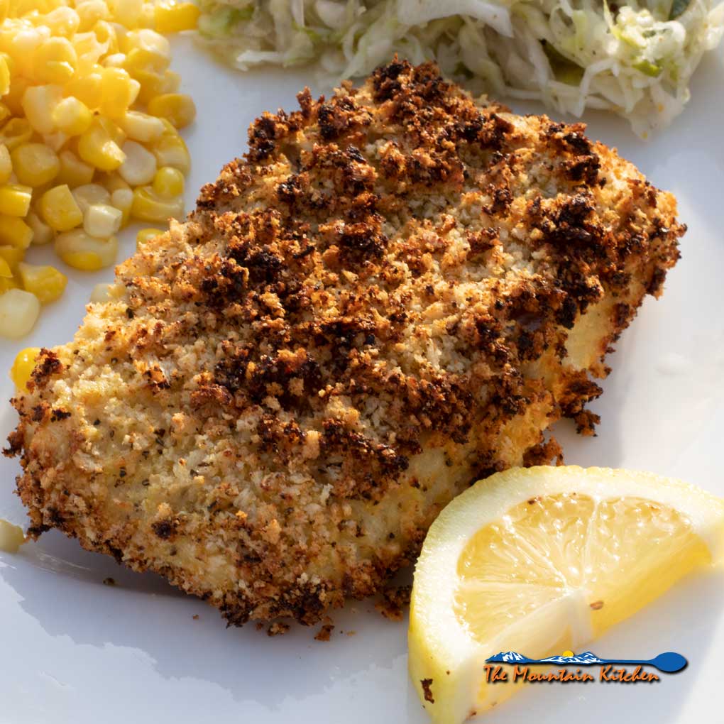 prepared air fryer cod on plate with lemon wedge, corn and slaw