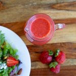 strawberry vinaigrette in glass pitcher with salad and strawberries