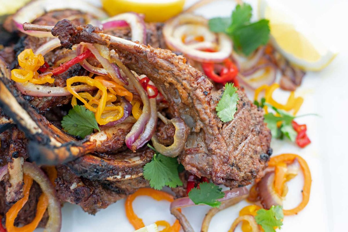 tandoori lamb chop on platter with onions, peppers, lemon wedges and cilantro