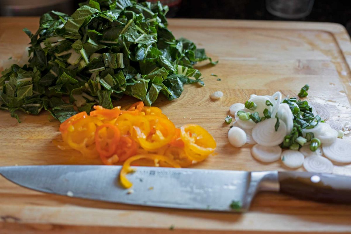 chopped bok choy, onion and mini peppers on cutting board with knife
