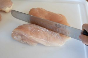 knife cutting whole chicken breast in half