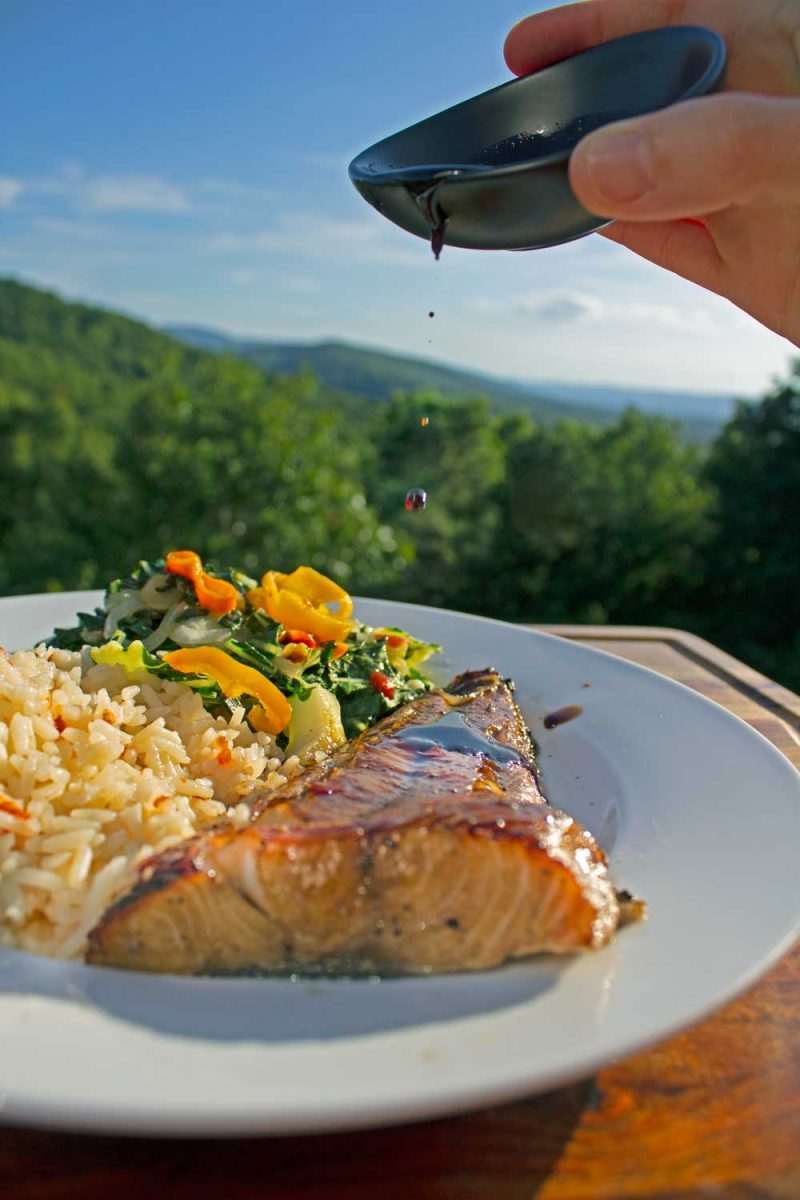 drizzling soy glaze onto plate of cod with mountain view