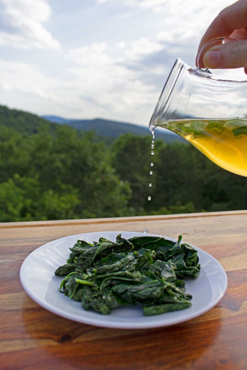 drizzling spring onion vinegar onto sauteed kale with mountain view